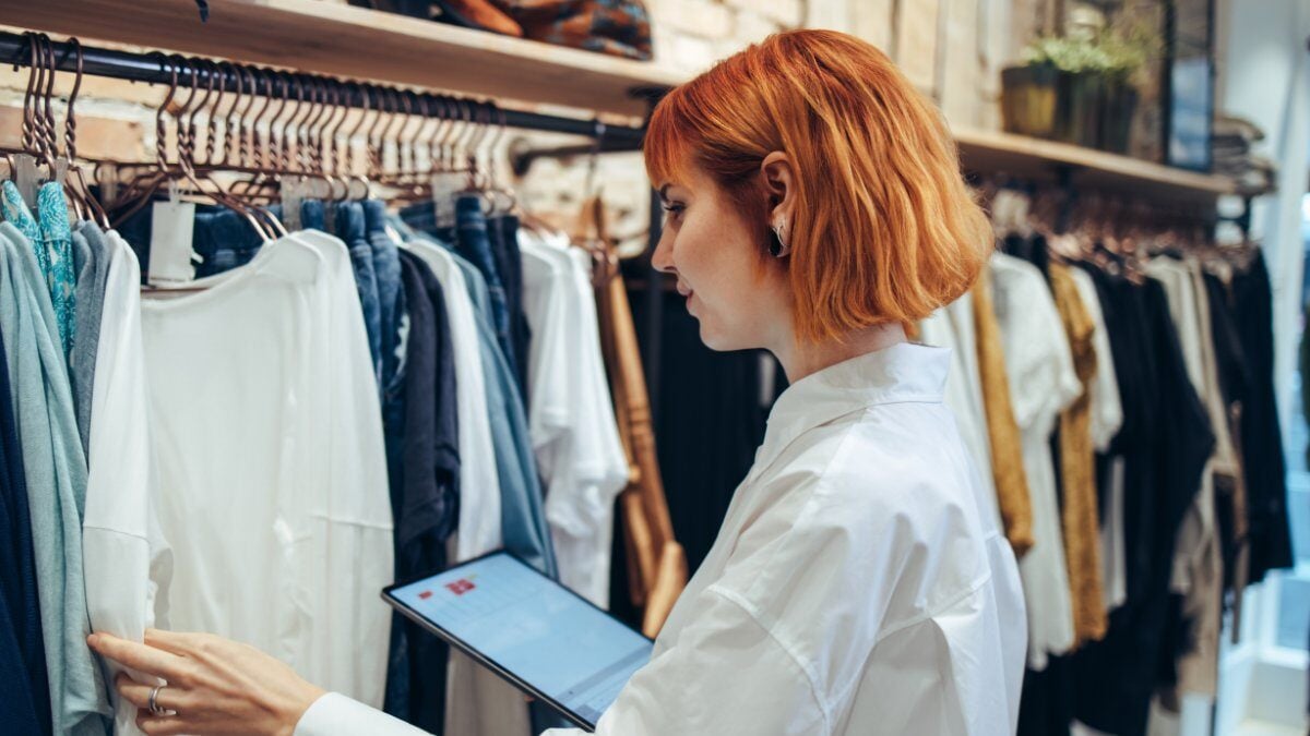 A store associate rearranging garments on display while holding an ipad